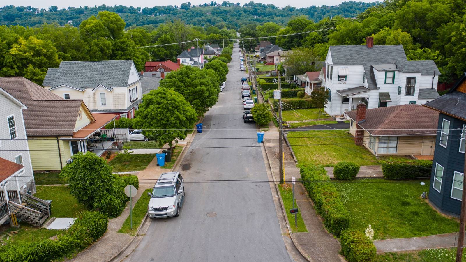 Aerial view of a residential street lined with houses, trees and parked cars