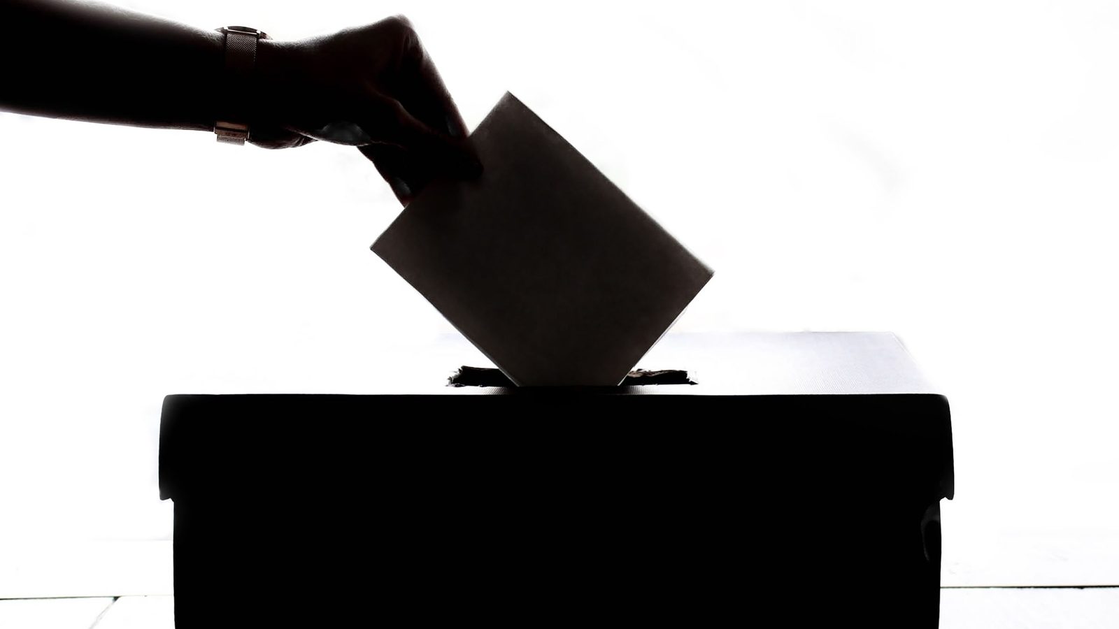 Silhouette of a hand dropping a ballot into a ballot box