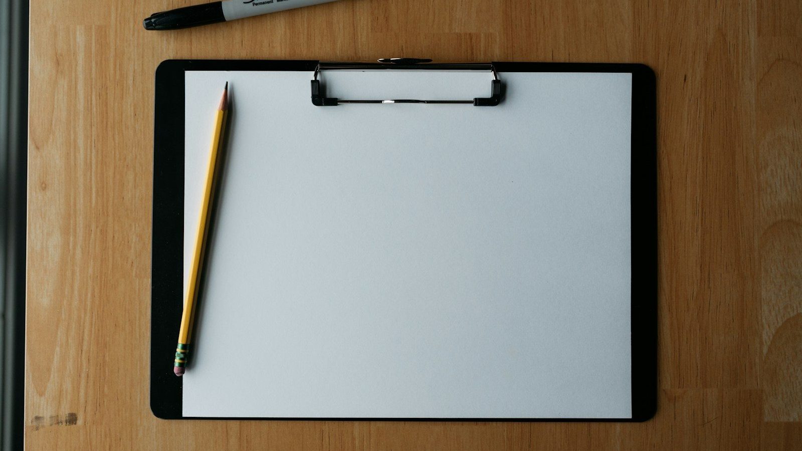 A blank clipboard and a pencil on a wooden table
