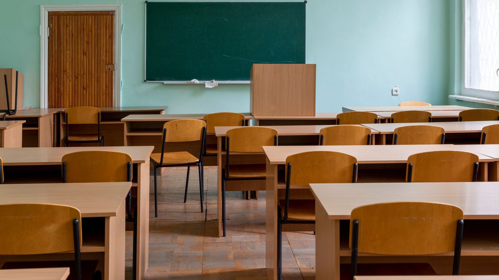An empty classroom with wooden desks and chairs facing a green chalkboard