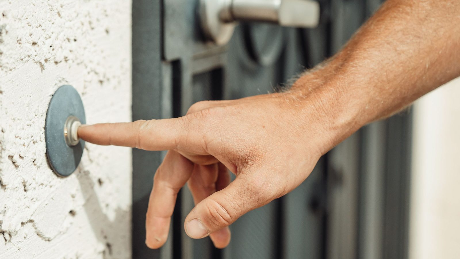 A finger presses a doorbell beside a front door