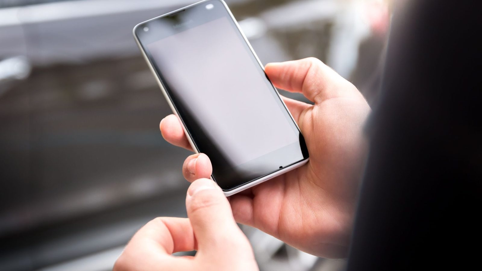 Two hands holding a smartphone outdoors