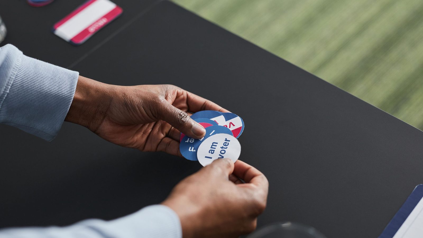 Hands holding round stickers that read I am a voter over a table