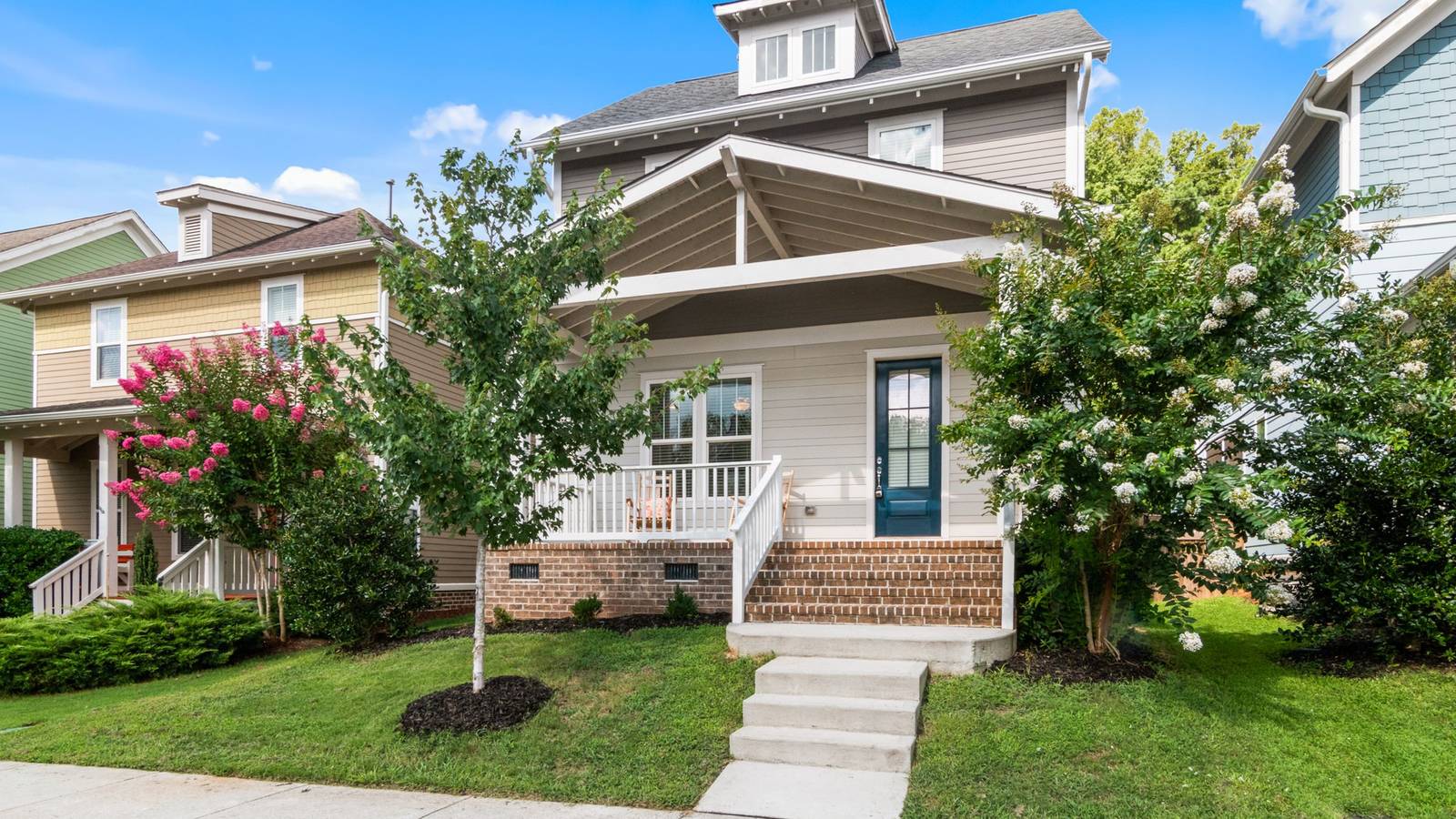 A two-story house with a front porch, brick steps and flowering trees