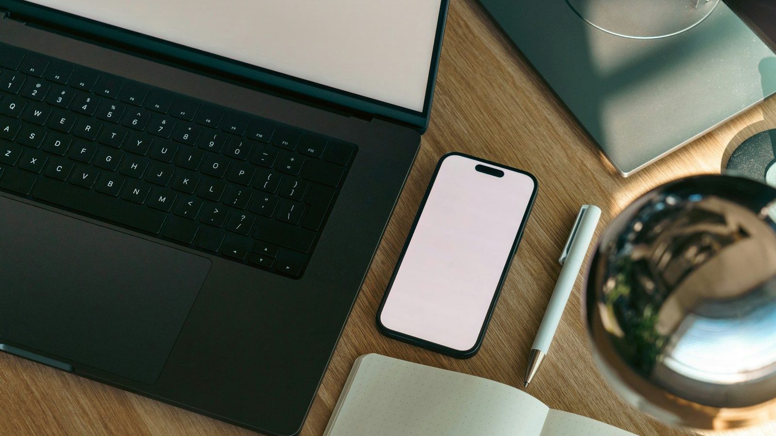 A laptop, a phone and a notebook on a wooden desk
