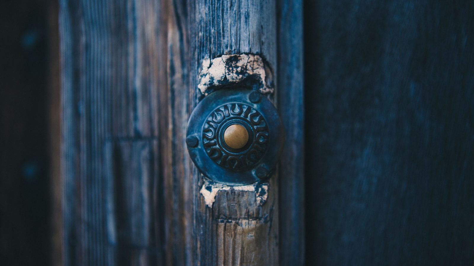 An old brass doorbell on a weathered blue wooden door