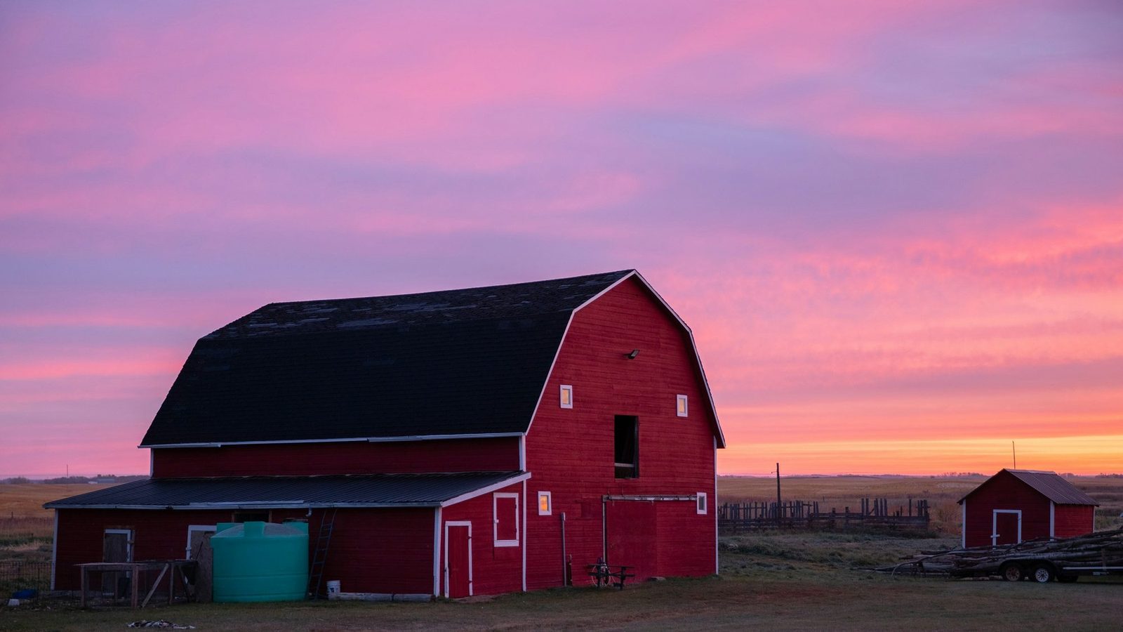 A red barn in an open field under a pink and purple sunset