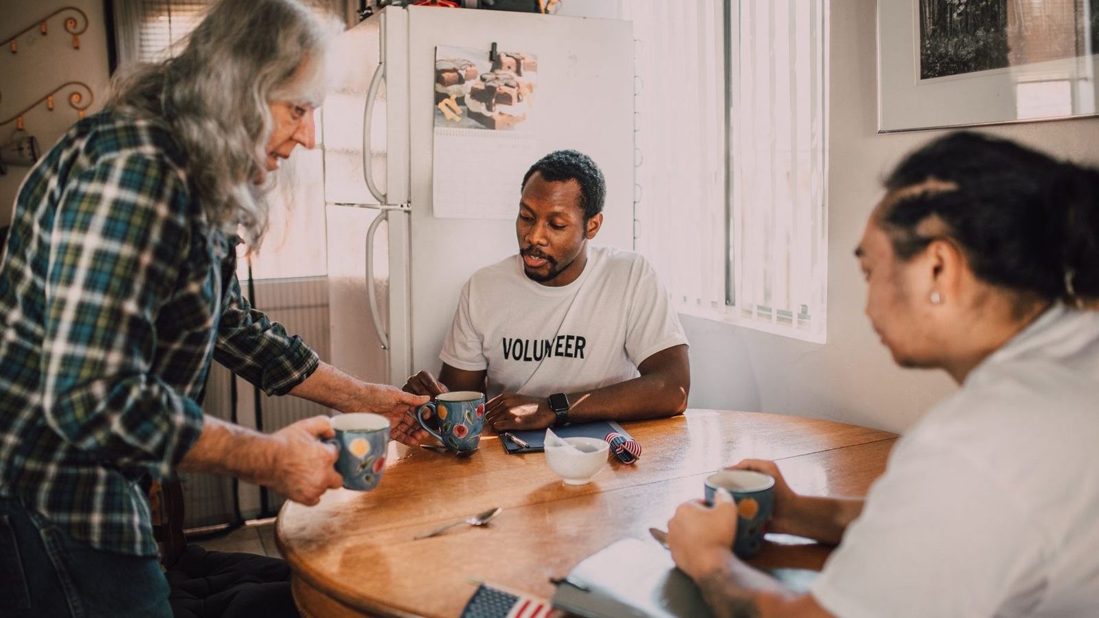 Three volunteers talking over coffee at a kitchen table