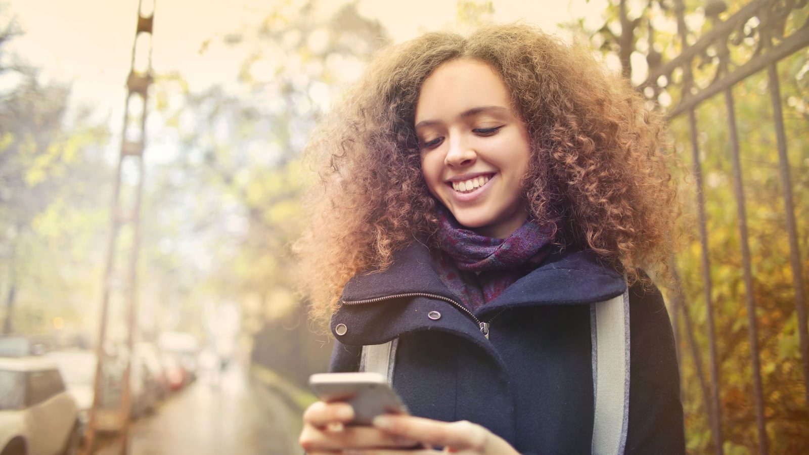 A smiling woman in a winter coat looks at her phone outdoors