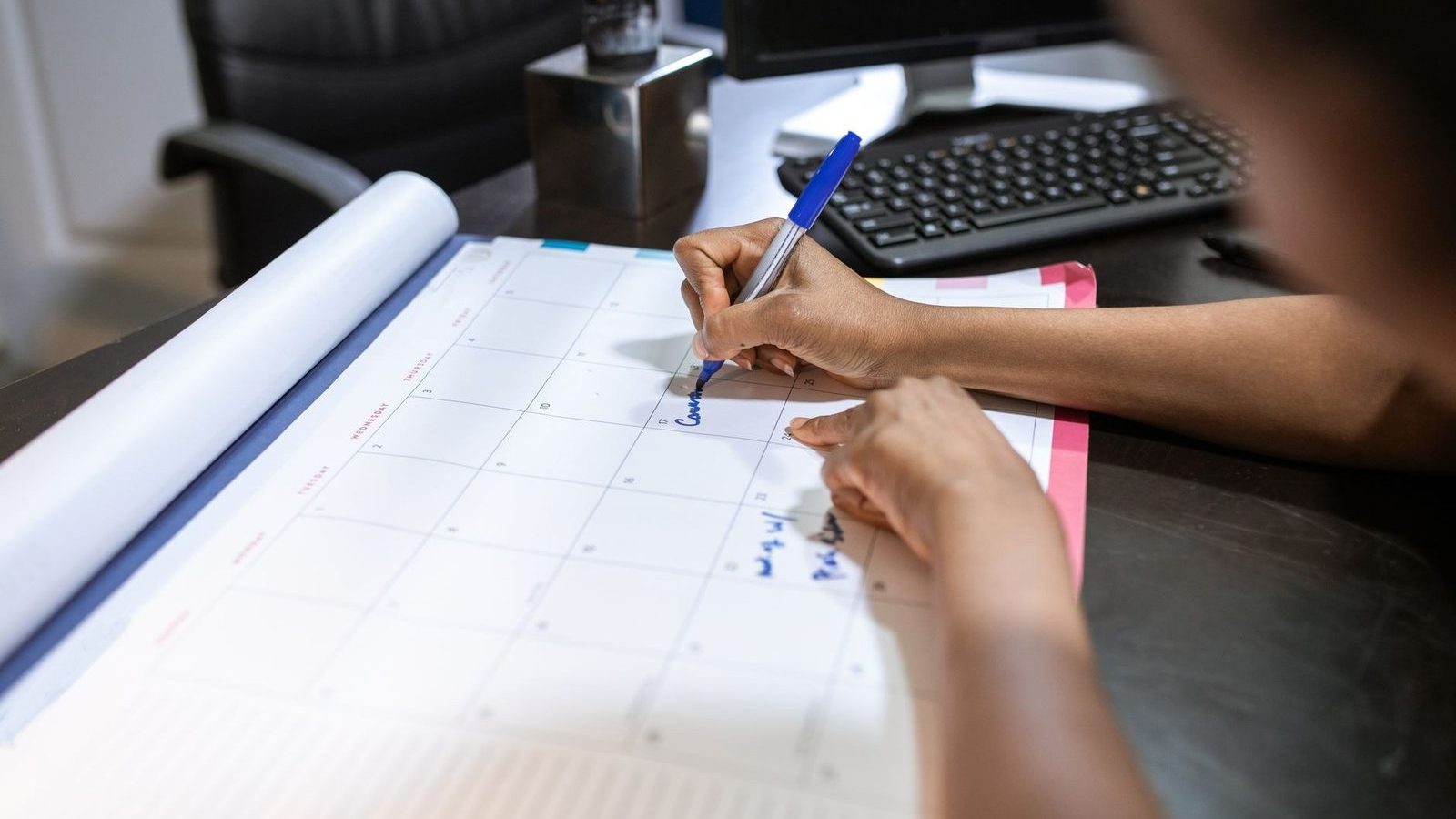 A person writing on a large desk calendar